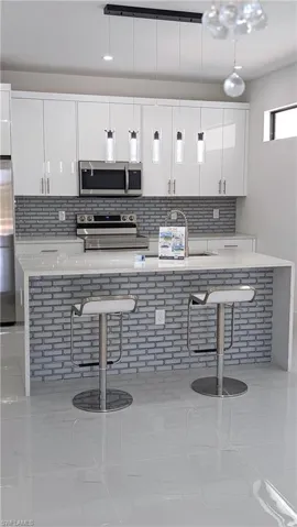 Kitchen with white cabinetry, a kitchen breakfast bar, tasteful backsplash, and stainless steel appliances