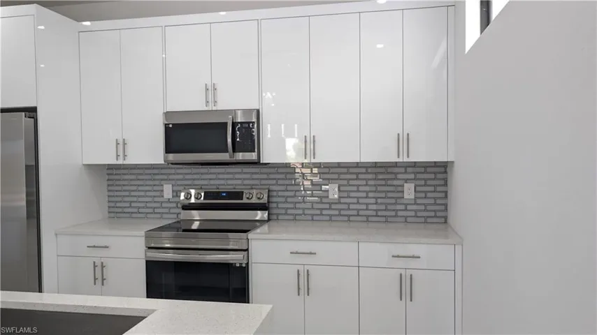 Kitchen with appliances with stainless steel finishes, white cabinetry, backsplash, and light stone counters