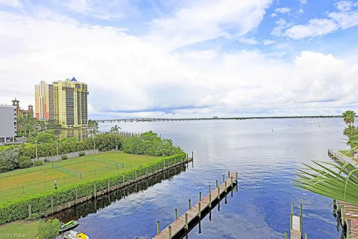 Expansive waterfront setting featuring a multi-story residential building, a long pier extending into the water, and a broad body of water with a distant bridge