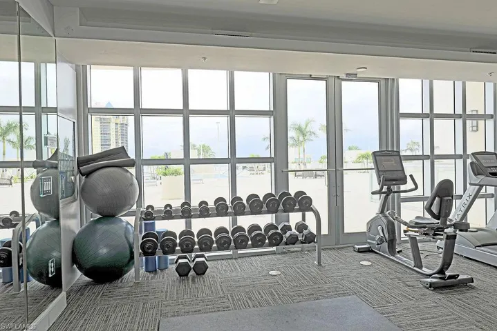 Fitness center featuring floor-to-ceiling windows, patterned carpet flooring, a mirrored wall, a dumbbell rack, and exercise equipment