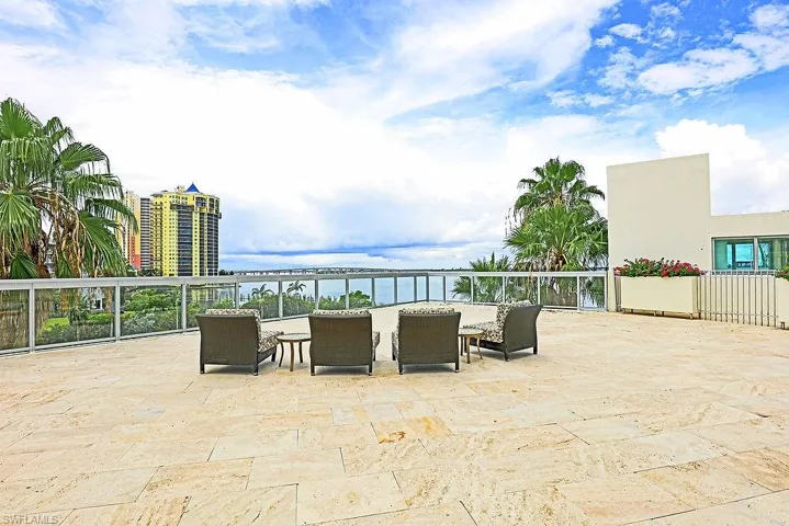 Expansive tiled patio featuring a glass railing system and water backdrop