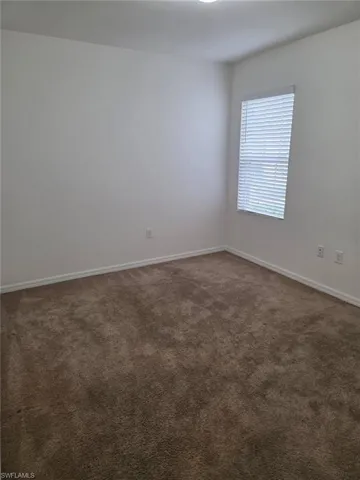 Spare room featuring dark colored carpet and baseboards