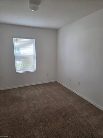 Spare room featuring dark colored carpet and baseboards