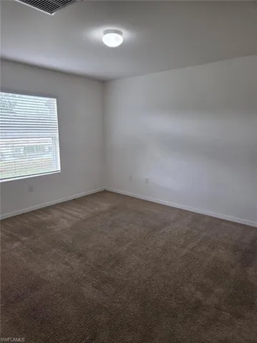 Unfurnished room featuring dark colored carpet and baseboards