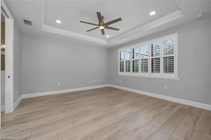 Empty room with a ceiling fan, light wood-style flooring, recessed lighting, and a tray ceiling