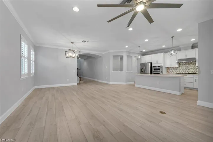 Unfurnished living room featuring ornamental molding, light wood finished floors, ceiling fan, arched walkways, and a chandelier