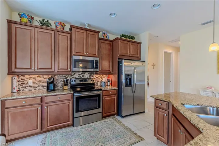Kitchen with decorative light fixtures, backsplash, appliances with stainless steel finishes, light tile patterned flooring, and light stone countertops