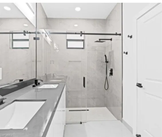 Full bath with double vanity, a marble finish shower, and recessed lighting