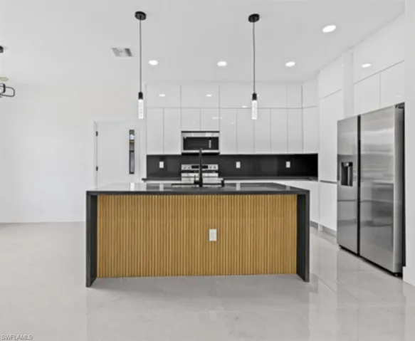 Kitchen featuring modern cabinets, appliances with stainless steel finishes, a spacious island, white cabinetry, and pendant lighting