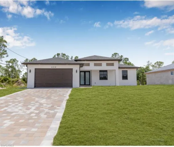 Prairie-style home with decorative driveway, a front yard, an attached garage, and stucco siding