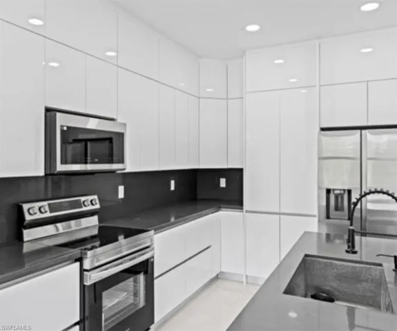 Kitchen with modern cabinets, stainless steel appliances, white cabinetry, recessed lighting, and backsplash