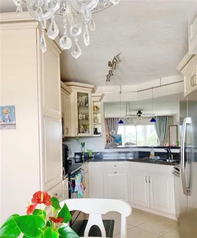 Kitchen with decorative light fixtures, freestanding refrigerator, dark stone countertops, light tile patterned floors, and a textured ceiling