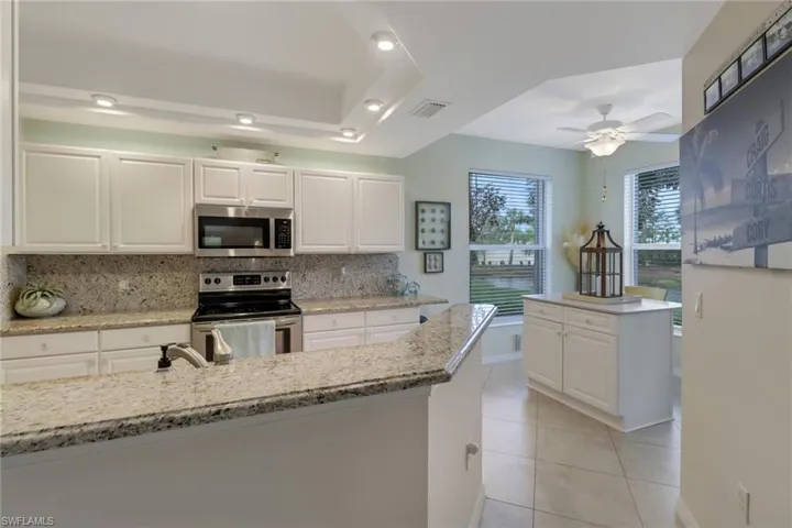 Kitchen featuring white cabinets, stainless steel appliances, a ceiling fan, light stone countertops, and a tray ceiling