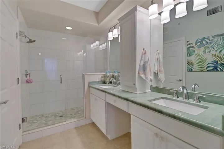 Bathroom with double vanity, a shower stall, and light tile patterned floors