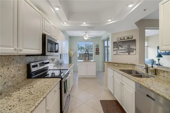 Kitchen featuring stainless steel appliances, white cabinetry, light stone counters, a ceiling fan, and a tray ceiling