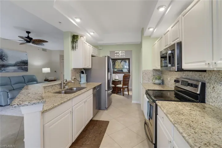 Kitchen featuring stainless steel appliances, white cabinetry, light stone counters, ceiling fan, and decorative backsplash