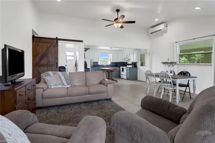 Tiled living room featuring a barn door, a wall mounted AC, ceiling fan, and vaulted ceiling