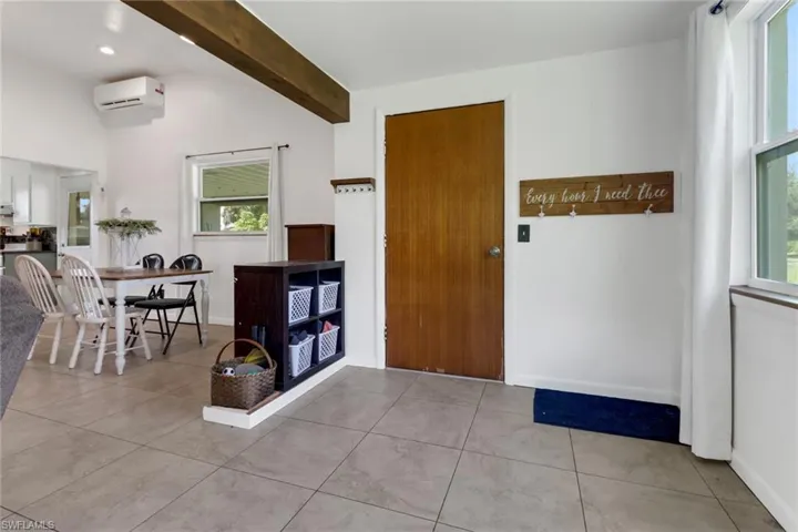 Entrance foyer featuring a wall unit AC, light tile patterned flooring, and vaulted ceiling with beams