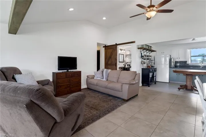 Living room with light tile patterned floors, high vaulted ceiling, ceiling fan, and a barn door