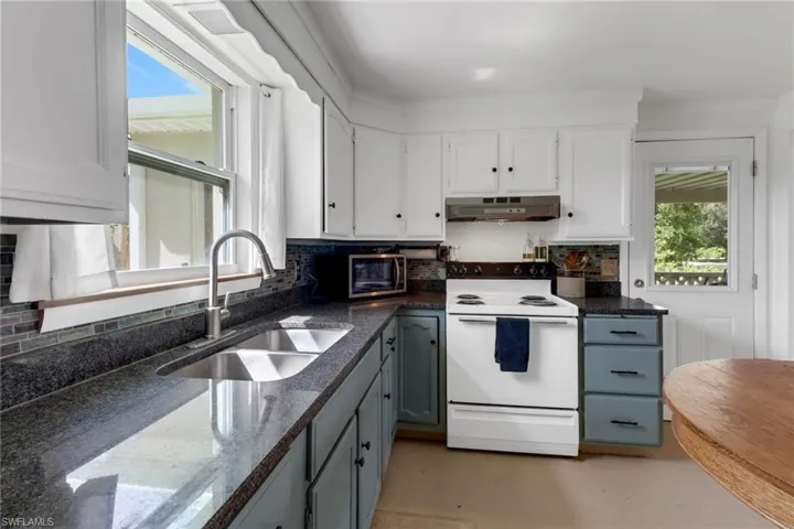 Kitchen with white electric stove, backsplash, sink, and white cabinets