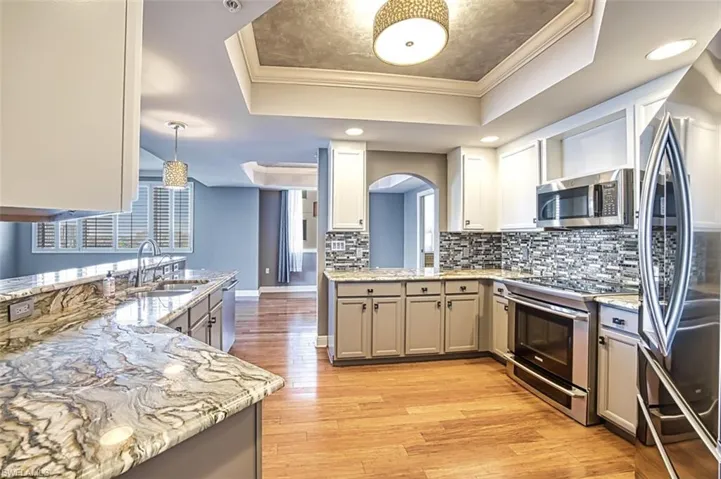 Kitchen with a tray ceiling, stainless steel appliances, ornamental molding, light wood finished floors, and light stone countertops