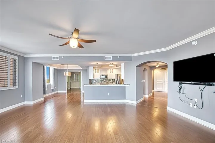 Unfurnished living room with ceiling fan, wood-type flooring, ornamental molding, and arched walkways