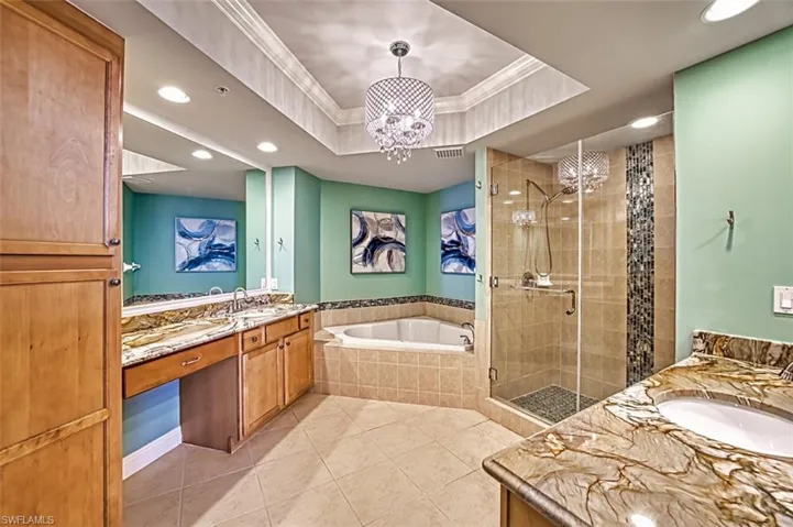 Bathroom with two vanities, a raised ceiling, a bath, a shower stall, and crown molding
