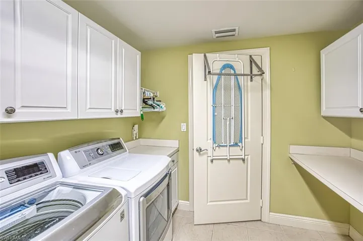 Laundry room with washer and clothes dryer, light tile patterned floors, and cabinet space