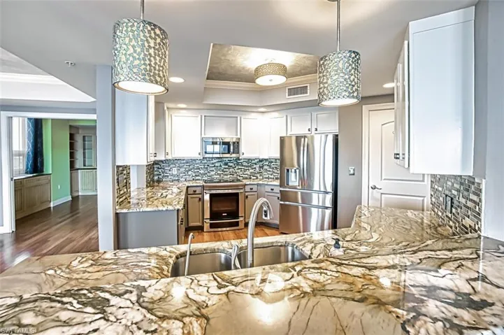 Kitchen with ornamental molding, pendant lighting, stainless steel appliances, light stone countertops, and tasteful backsplash
