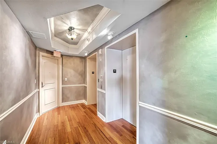 Hallway featuring elevator, a tray ceiling, wood finished floors, and ornamental molding