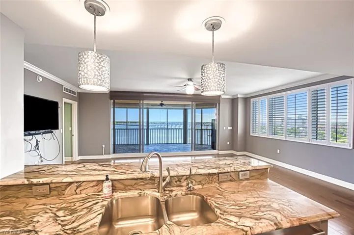 Kitchen with light stone countertops, crown molding, decorative light fixtures, wood finished floors, and a ceiling fan