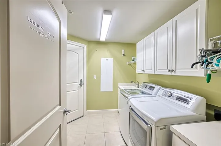 Laundry area with light tile patterned floors, washing machine and dryer, and cabinet space
