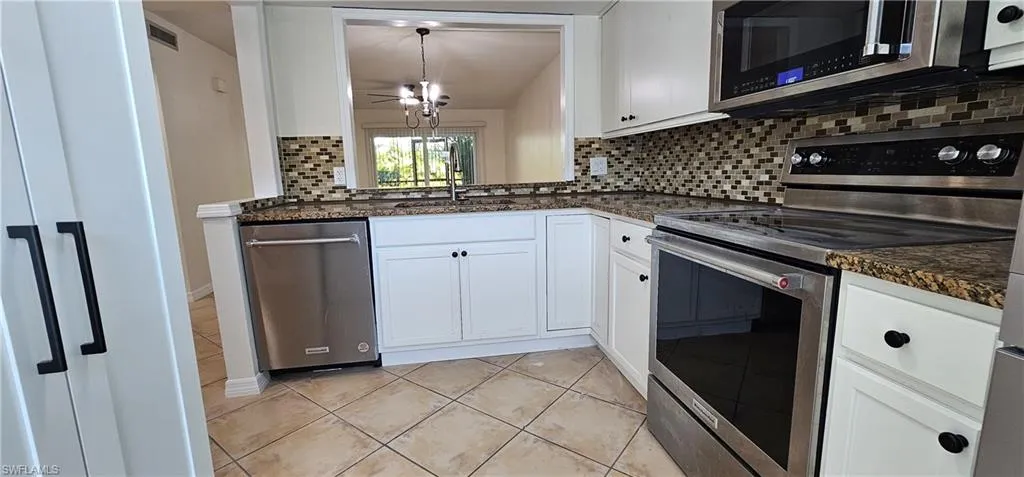 Kitchen with stainless steel appliances, white cabinets, pendant lighting, backsplash, and light tile patterned floors