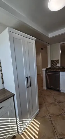 Kitchen featuring white cabinets, stainless steel dishwasher, tasteful backsplash, and light tile patterned floors