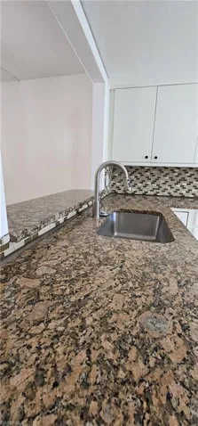 Kitchen featuring backsplash, dark stone counters, and white cabinetry