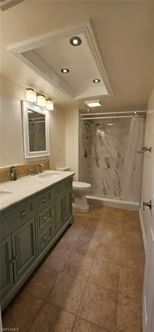 Full bathroom with a marble finish shower, double vanity, recessed lighting, and a tray ceiling