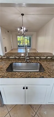 Kitchen featuring white cabinetry, light tile patterned floors, dark stone countertops, and decorative light fixtures