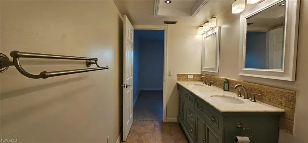 Bathroom featuring double vanity, dark tile patterned flooring, and backsplash