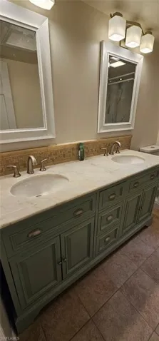 Full bath with double vanity, backsplash, dark tile patterned floors, and a shower