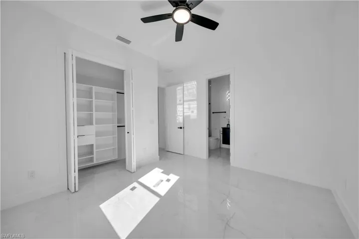Unfurnished bedroom featuring light marble finish floors, ceiling fan, ensuite bathroom, and a closet