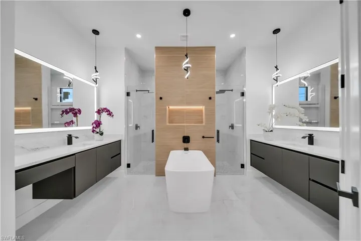 Full bath with two vanities, a stall shower, a freestanding bath, and recessed lighting