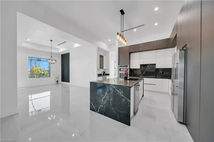 Kitchen featuring modern cabinets, decorative light fixtures, a kitchen island with sink, dark stone countertops, and a raised ceiling