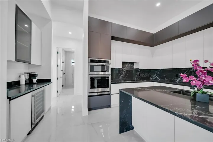 Kitchen with modern cabinets, white cabinets, dark stone counters, recessed lighting, and wine cooler