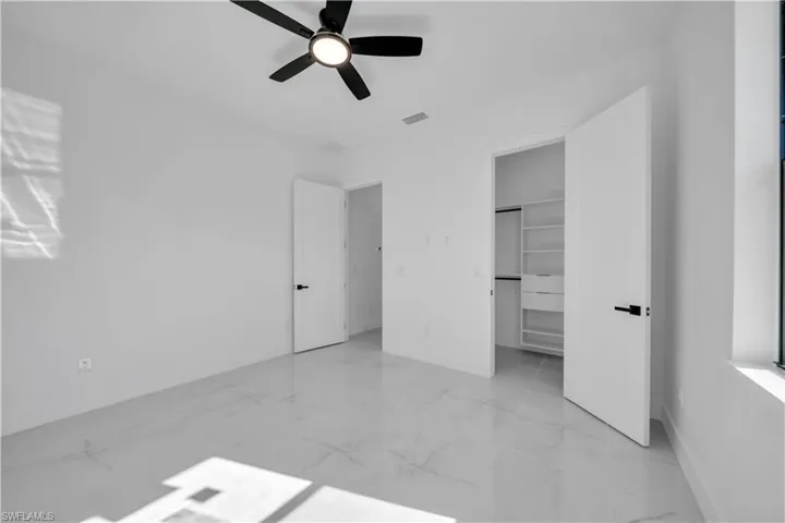 Unfurnished bedroom with a walk in closet, ceiling fan, and light marble finish floors