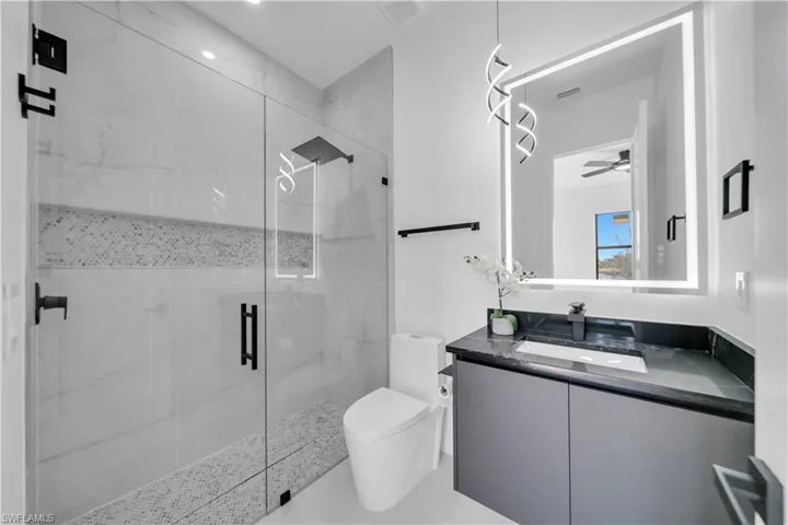Full bath with vanity, a marble finish shower, and ceiling fan