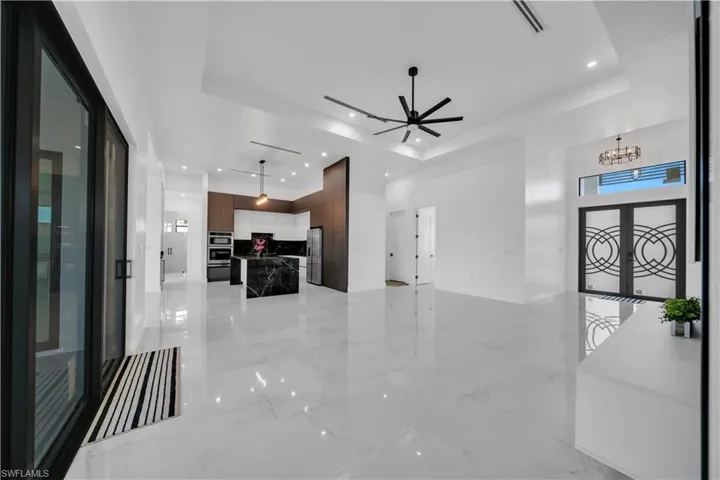Unfurnished living room featuring light marble finish flooring, a ceiling fan, french doors, hanging lights, and a raised ceiling