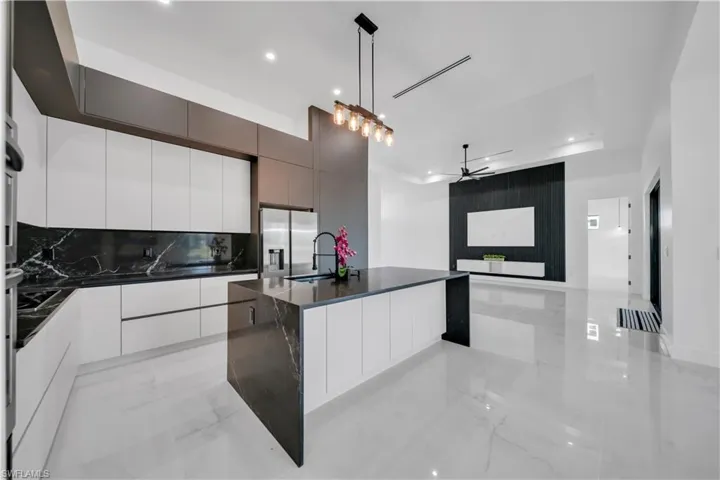 Kitchen featuring modern cabinets, an island with sink, white cabinets, ceiling fan, and dark stone counters