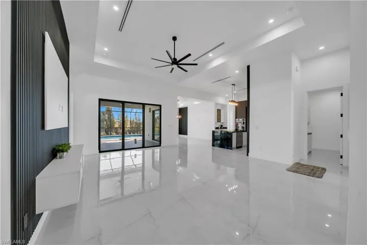 Unfurnished living room with light marble finish floors, recessed lighting, a raised ceiling, and a ceiling fan