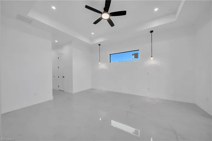 Empty room with a tray ceiling, recessed lighting, a ceiling fan, and light marble finish floors