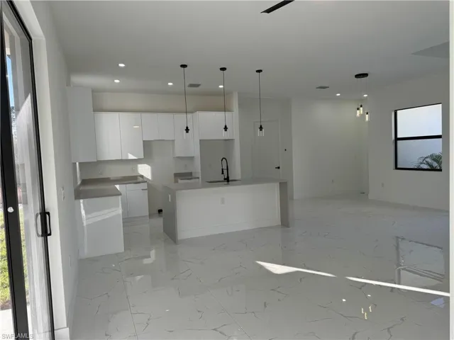 Kitchen featuring sink, a center island with sink, white cabinets, and decorative light fixtures